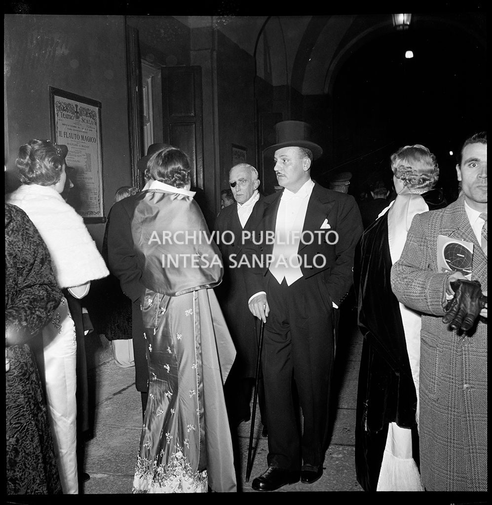 Lo stilista Pierre Balmain, tra la folla di spettatori, nella galleria delle carrozze del Teatro alla Scala la sera dell'inaugurazione della stagione lirica 1955-1956 con l'opera "Norma" di Vincenzo Bellini, diretta da Antonino Votto con la regia di Margherita Wallmann