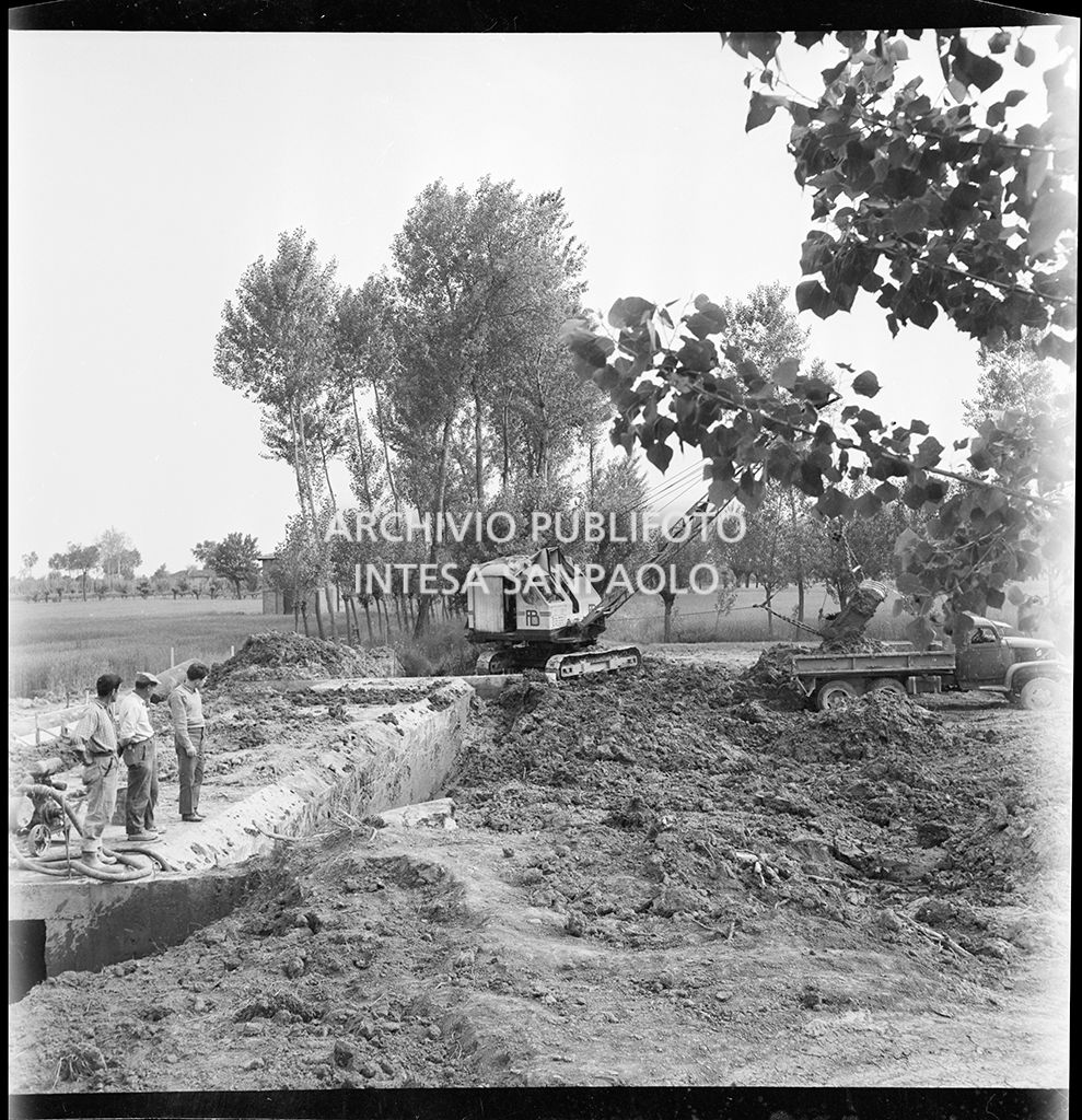 Tre uomini osservano l'escavatrice al lavoro nel cantiere di costruzione dell'Autostrada del Sole nei pressi di Fontanellato, tratto Fidenza-Parma<br>383281
