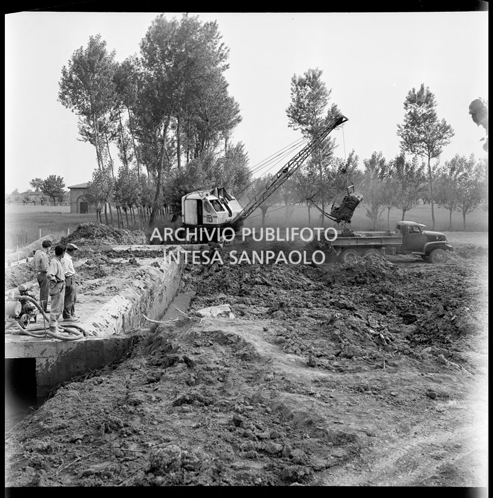 Tre uomini osservano l'escavatrice al lavoro nel cantiere di costruzione dell'Autostrada del Sole nei pressi di Fontanellato, tratto Fidenza-Parma<br>383282