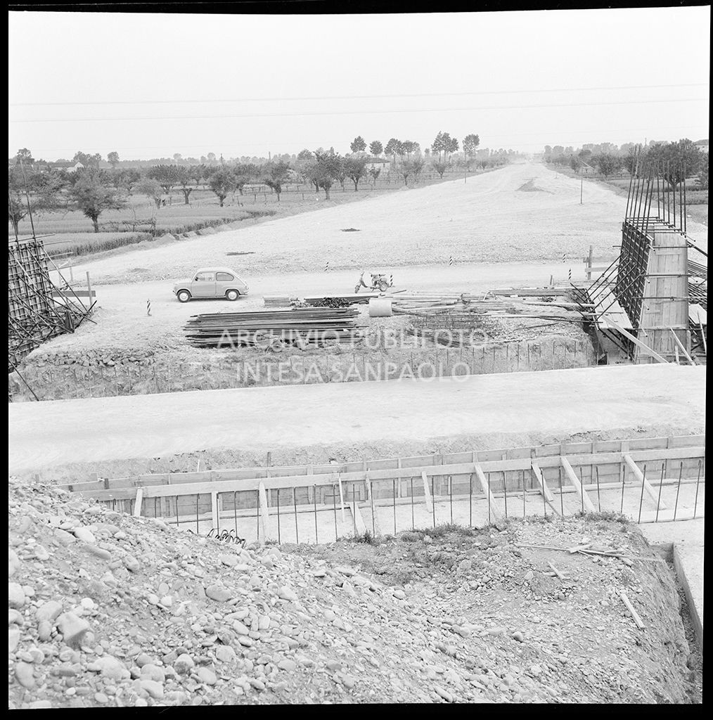 Cantiere di costruzione dell'Autostrada del Sole nei pressi di Parma: sullo sfondo una Fiat 600 e una Lambretta<br>383295
