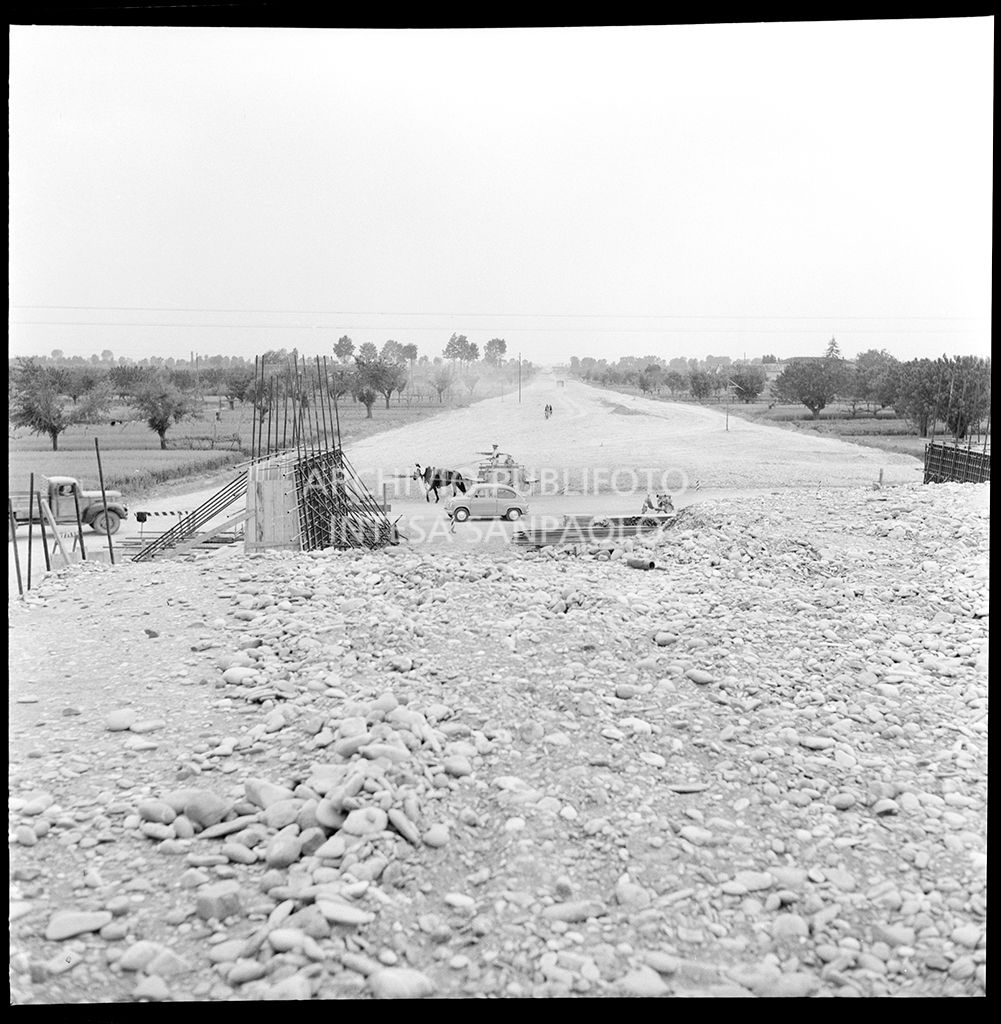 Cantiere di costruzione dell'Autostrada del Sole nei pressi di Parma; sullo sfondo un carro tirato da un mulo, una Fiat 600 e una Lambretta<br>383297