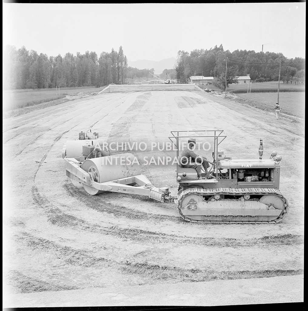 Un uomo al lavoro su un trattore che traina dei rulli compattatori 
					nel cantiere di costruzione dell'Autostrada del Sole, tratta Casalecchio di Reno-Sasso Marconi