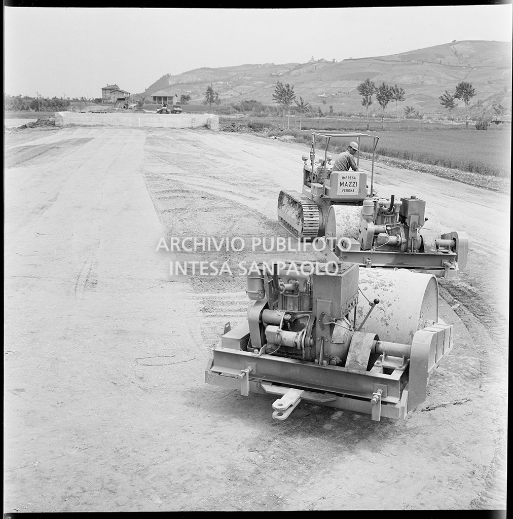 Un uomo al lavoro su un trattore che traina dei rulli compattatori
				nel cantiere di costruzione dell'Autostrada del Sole, tratta Casalecchio di Reno-Sasso Marconi<br>383299