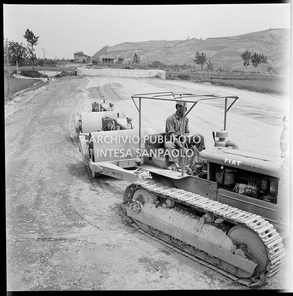 Un uomo al lavoro su un trattore che traina dei rulli compattatori
				nel cantiere di costruzione dell'Autostrada del Sole, tratta Casalecchio di Reno-Sasso Marconi<br>383305