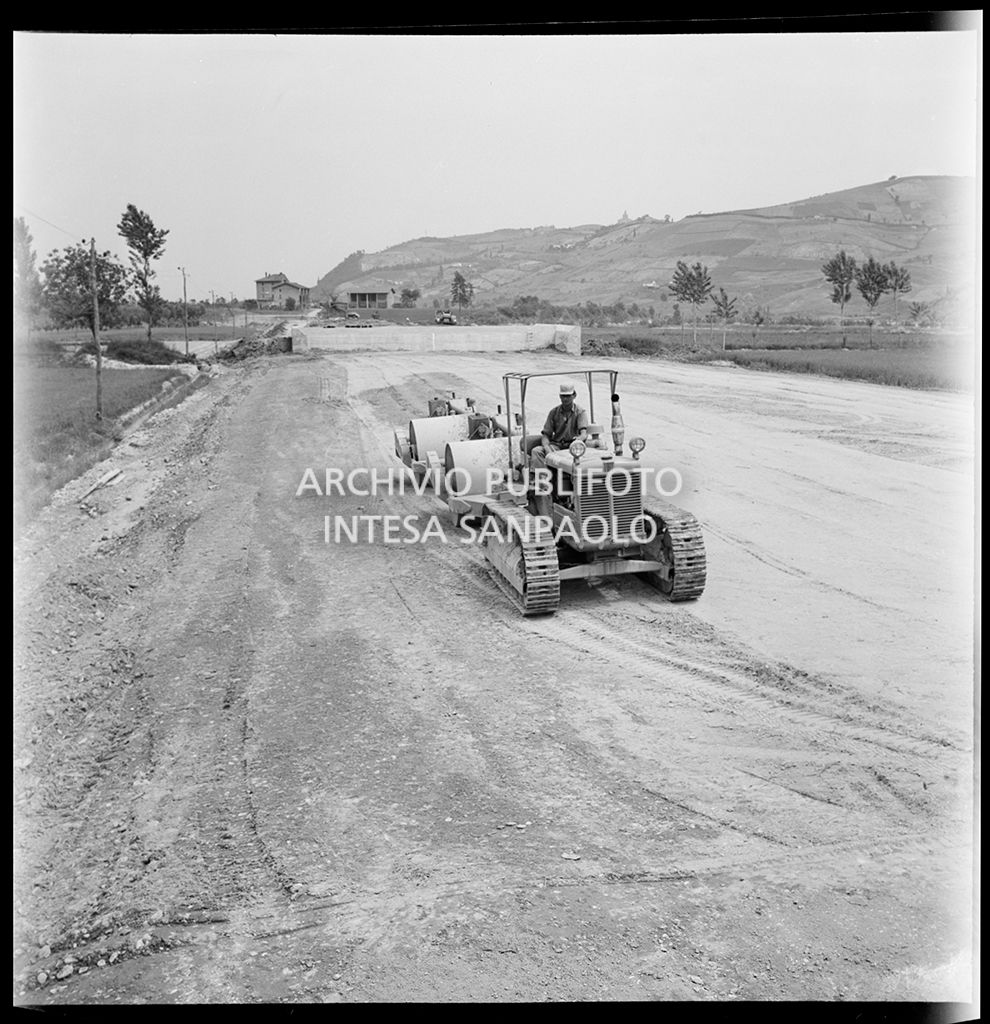 Un uomo al lavoro su un trattore che traina dei rulli compattatori
				nel cantiere di costruzione dell'Autostrada del Sole, tratta Casalecchio di Reno-Sasso Marconi<br>383306