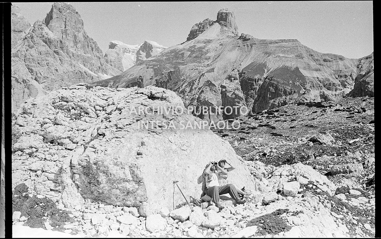 Due alpinisti scrutano con il binocolo la parete Nord della Cima ovest di Lavaredo
