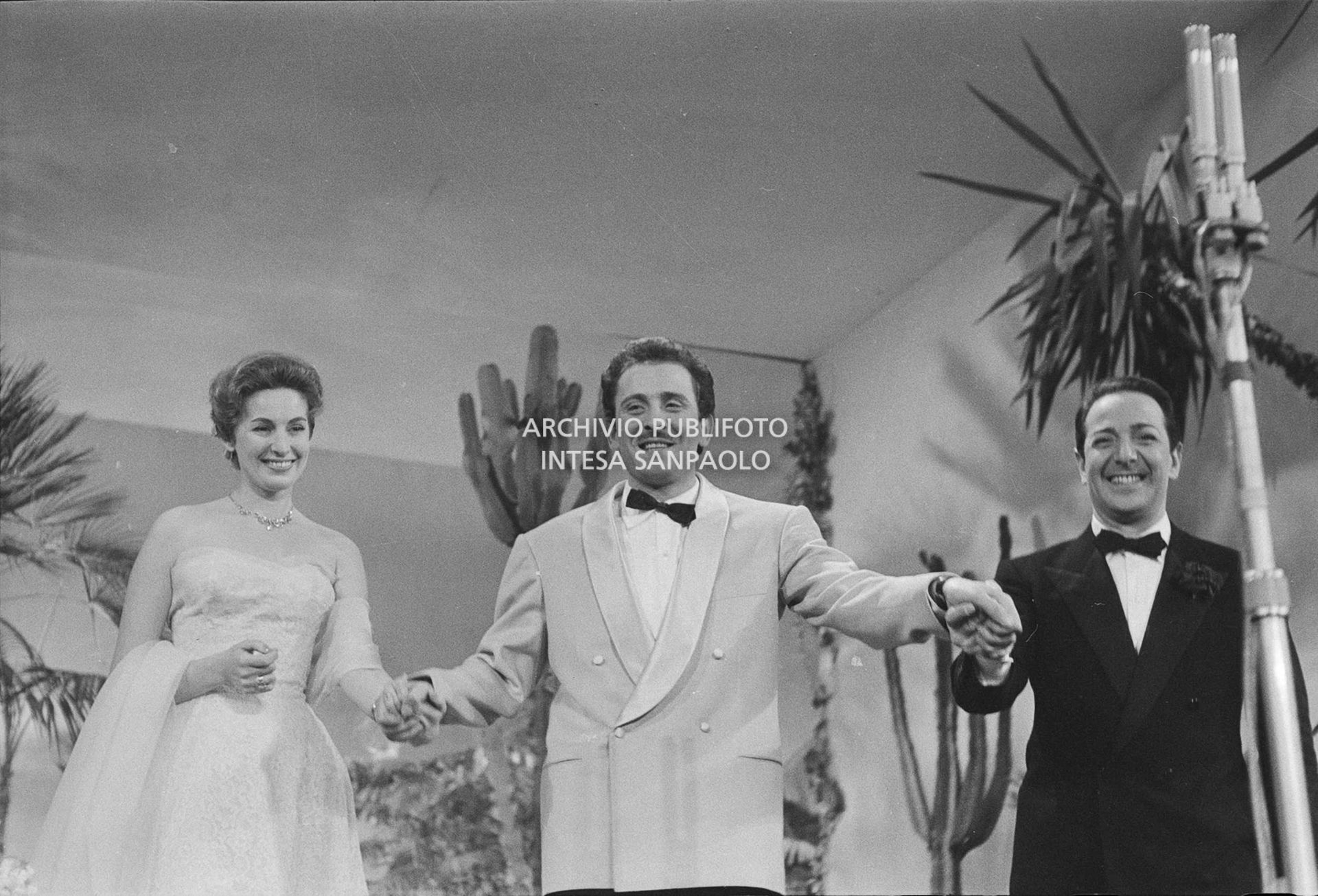 Domenico Modugno sul palco dell'VIII Festival della canzone italiana di Sanremo tra Gianni Agus, che conduce la competizione canora assistito da Fulvia Colombo