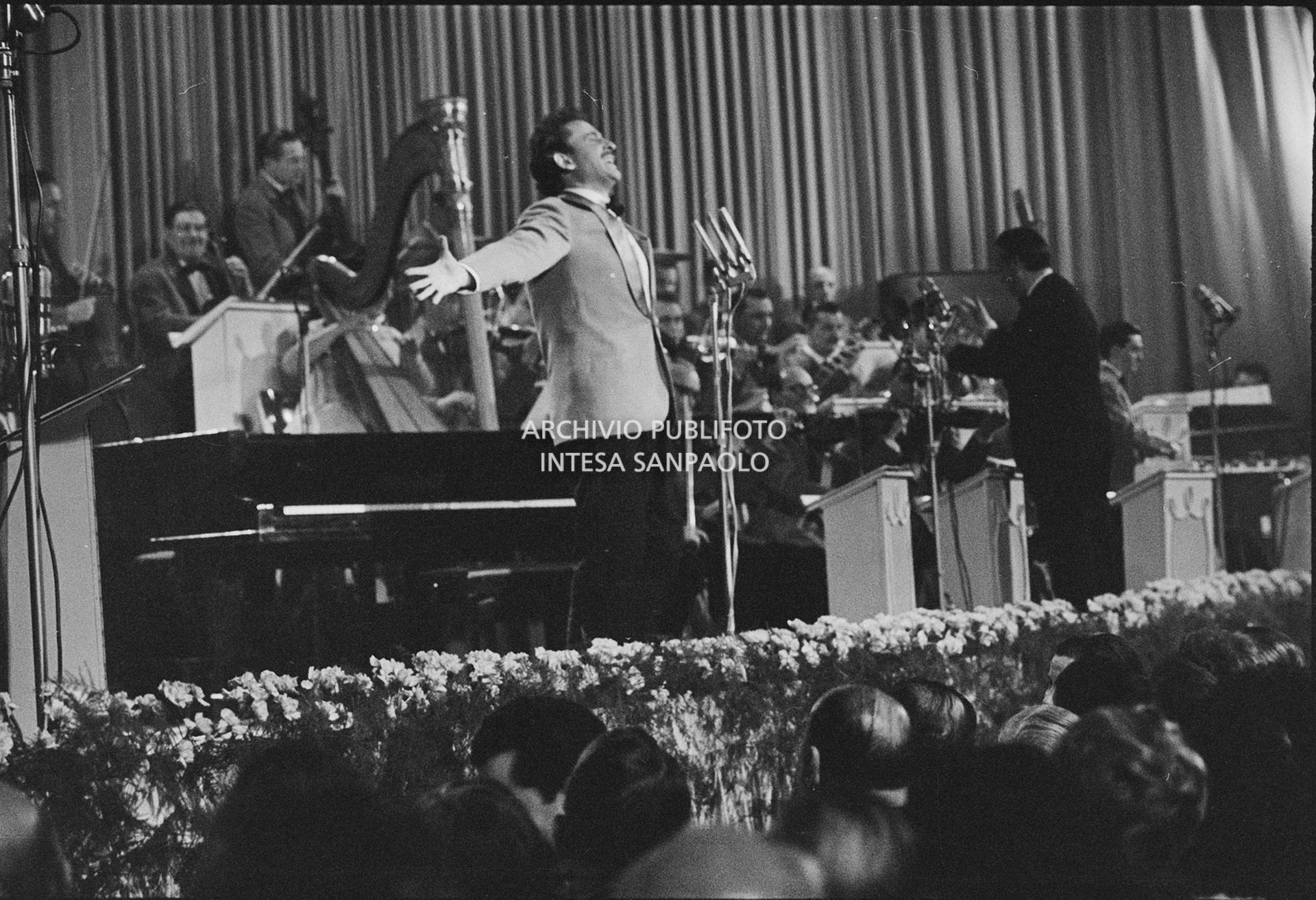 Domenico Modugno, si esibisce sul palco del Salone delle feste del Casinò al IX Festival di Sanremo, che vincerà, insieme a Johnny Dorelli, con la canzone "Piove"