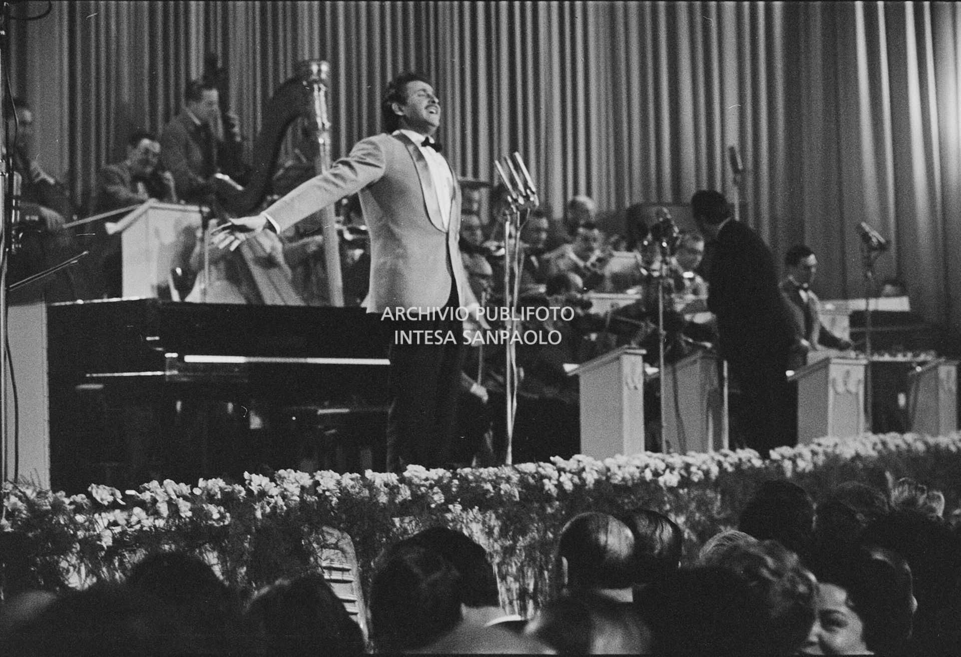 Domenico Modugno, si esibisce sul palco del Salone delle feste del Casinò al IX Festival di Sanremo, che vincerà, insieme a Johnny Dorelli, con la canzone "Piove"