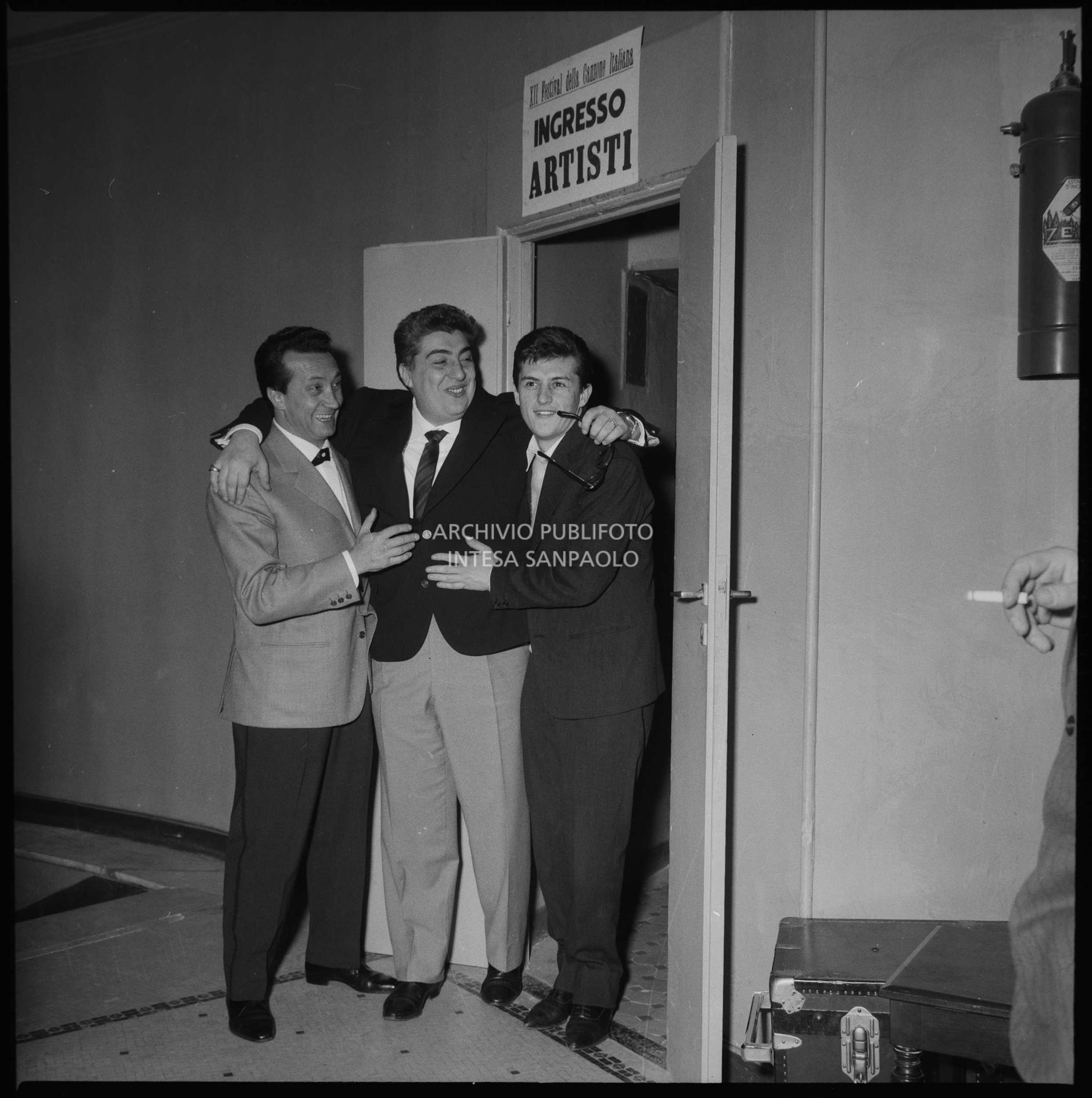 Ernesto Bonino, Gino Bramieri e Tony Renis si abbracciano davanti all'ingresso artisti all'interno del Casinò di Sanremo nei giorni del Festival
