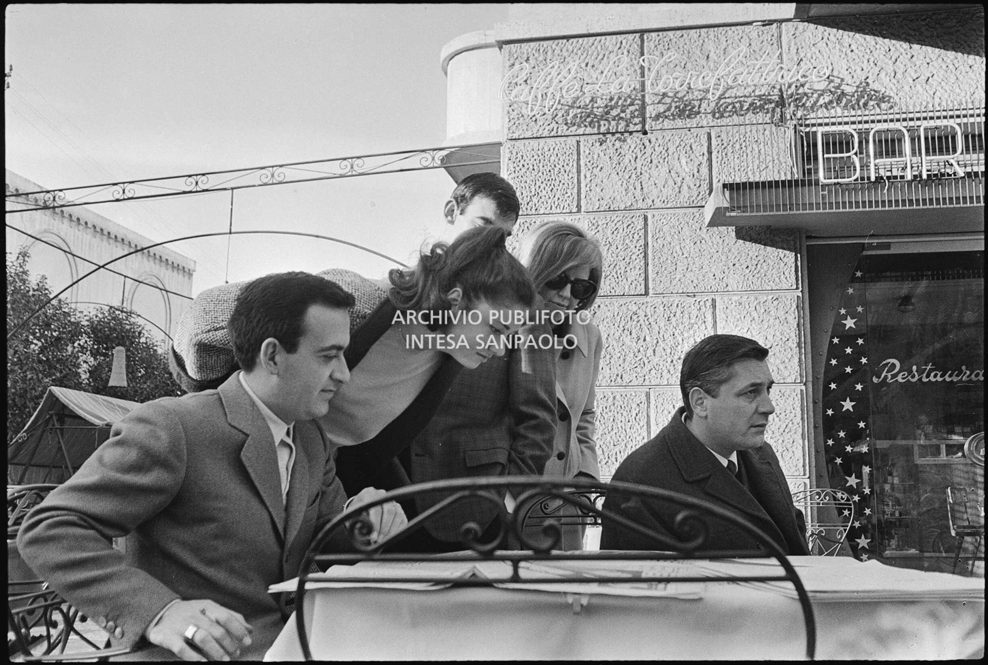 Cantanti, tra cui Gigliola Cinquetti, Piero Focaccia e Betty Curtis, al tavolino di un bar all'aperto a Sanremo nei giorni del XV Festival, leggono i giornali