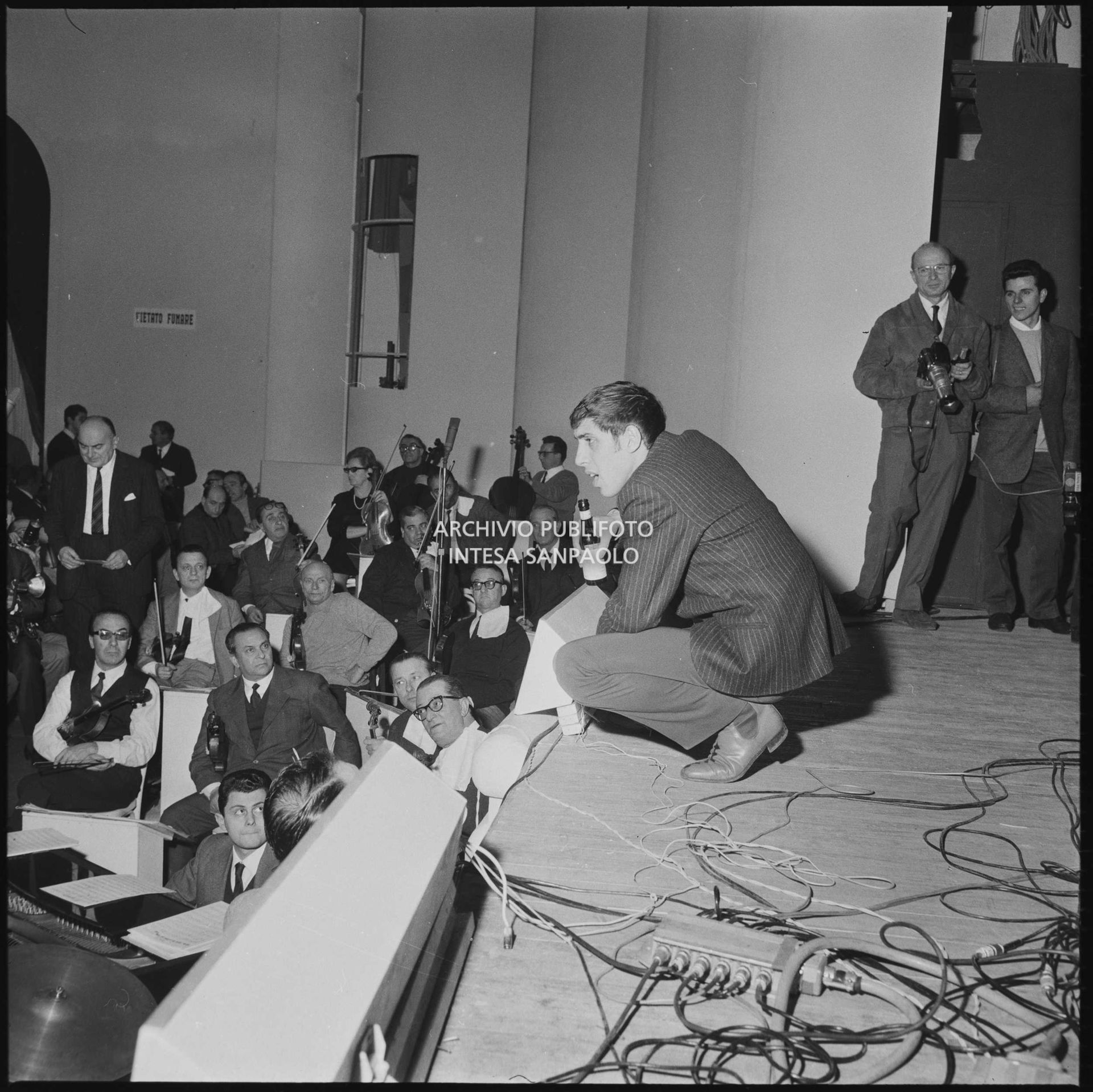 Adriano Celentano accosciato sul palco del salone delle feste del Casinò di Sanremo durante le prove