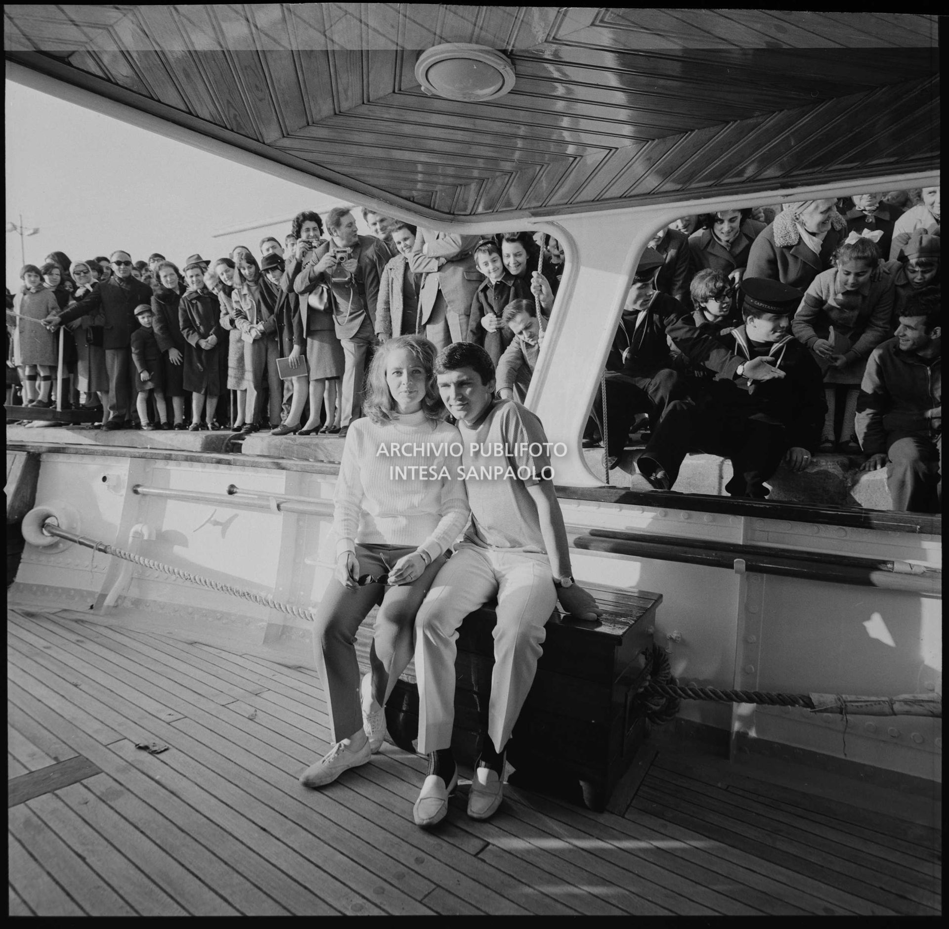 Gene Pitney e Lynne Gayton ritratti su uno yacht ormeggiato a Sanremo nei giorni del XVII Festival; sullo sfondo curiosi assiepati