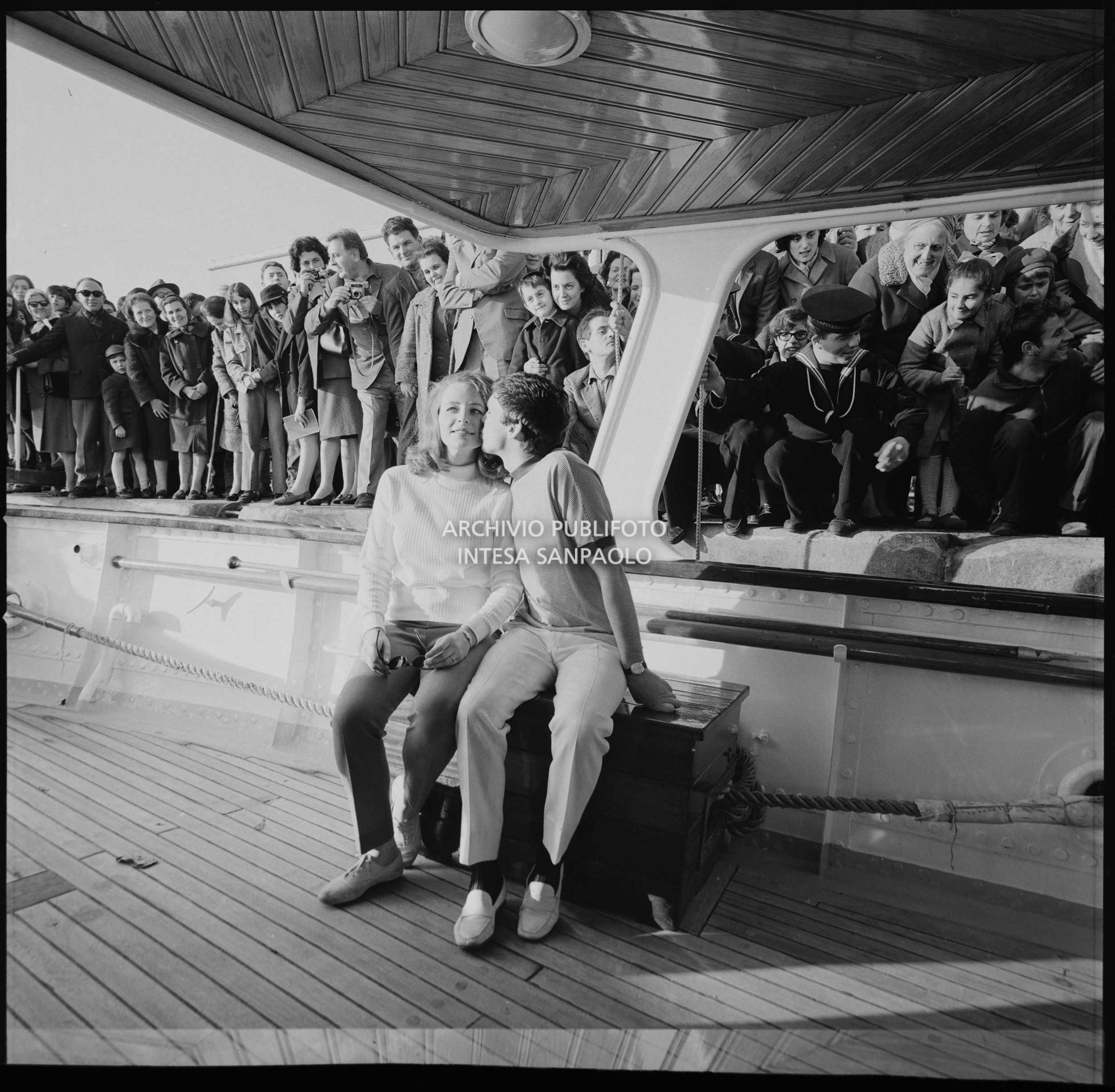 Gene Pitney e Lynne Gayton ritratti su uno yacht ormeggiato a Sanremo nei giorni del XVII Festival; sullo sfondo curiosi assiepati