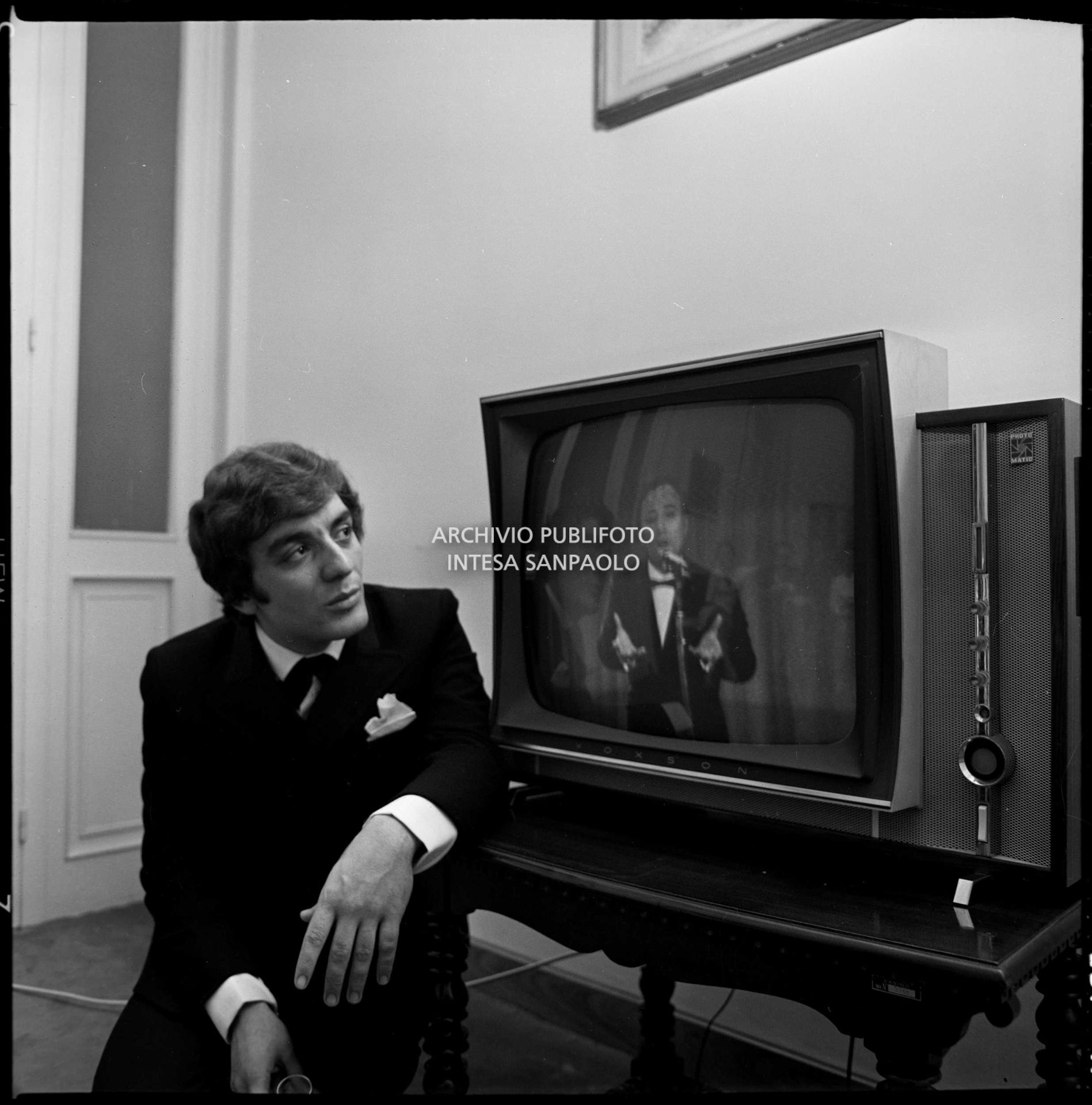 Mino Reitano ritratto mentre guarda la televisione dietro alla quinte del XIX Festival di Sanremo