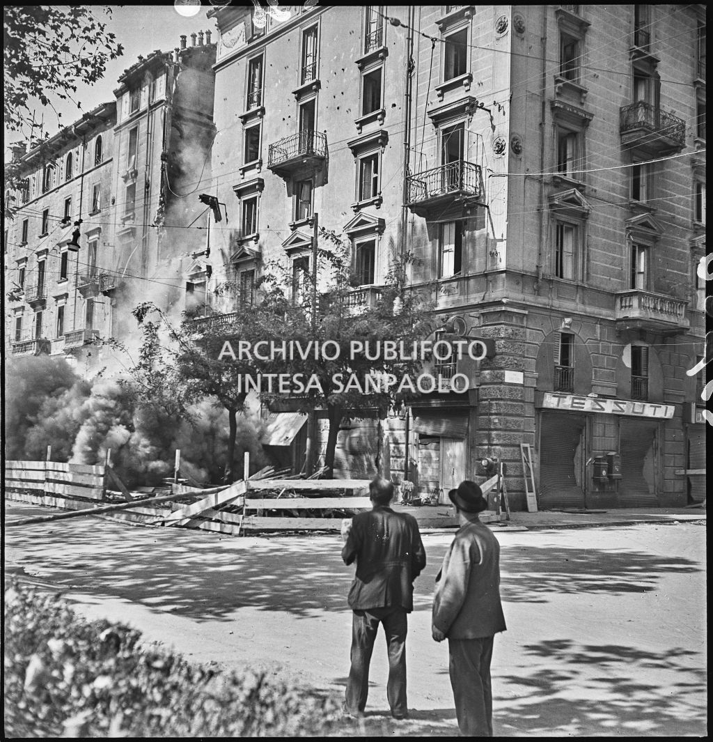 Demolizione di un edificio in via Vittorio Veneto angolo via Lecco, danneggiato dai bombardamenti; alcuni passanti osservano la scena