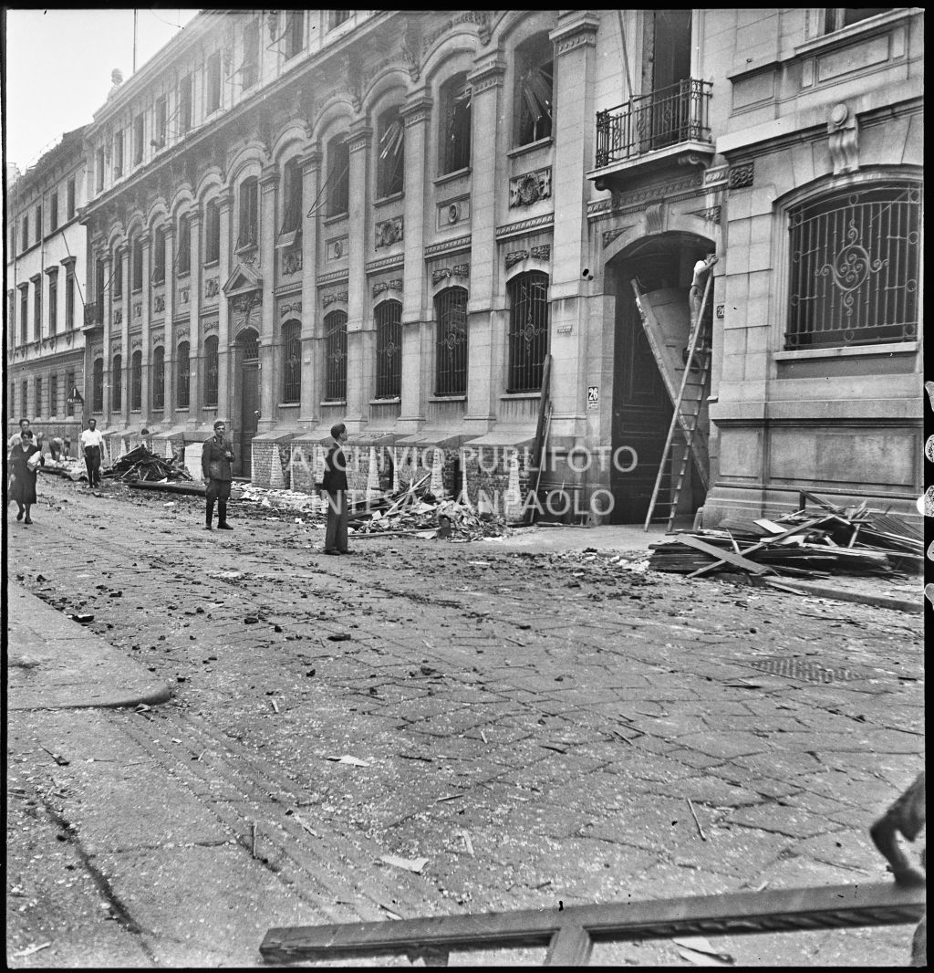 Scorcio di via Solferino con la sede del Corriere della Sera danneggiata dai bombardamenti, sono visibili macerie e persone lungo la strada