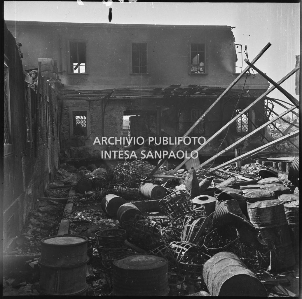 Panoramica del cortile interno dell'impresa Chiappetta danneggiata dai bombardamenti: a terra numerosi barili e macerie