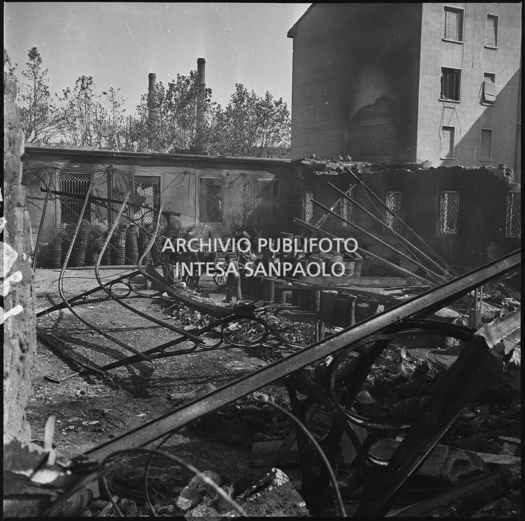 Persone al lavoro intente a recuperare materiali tra le macerie nel cortile interno dell'impresa Chiappetta danneggiata dai bombardamenti