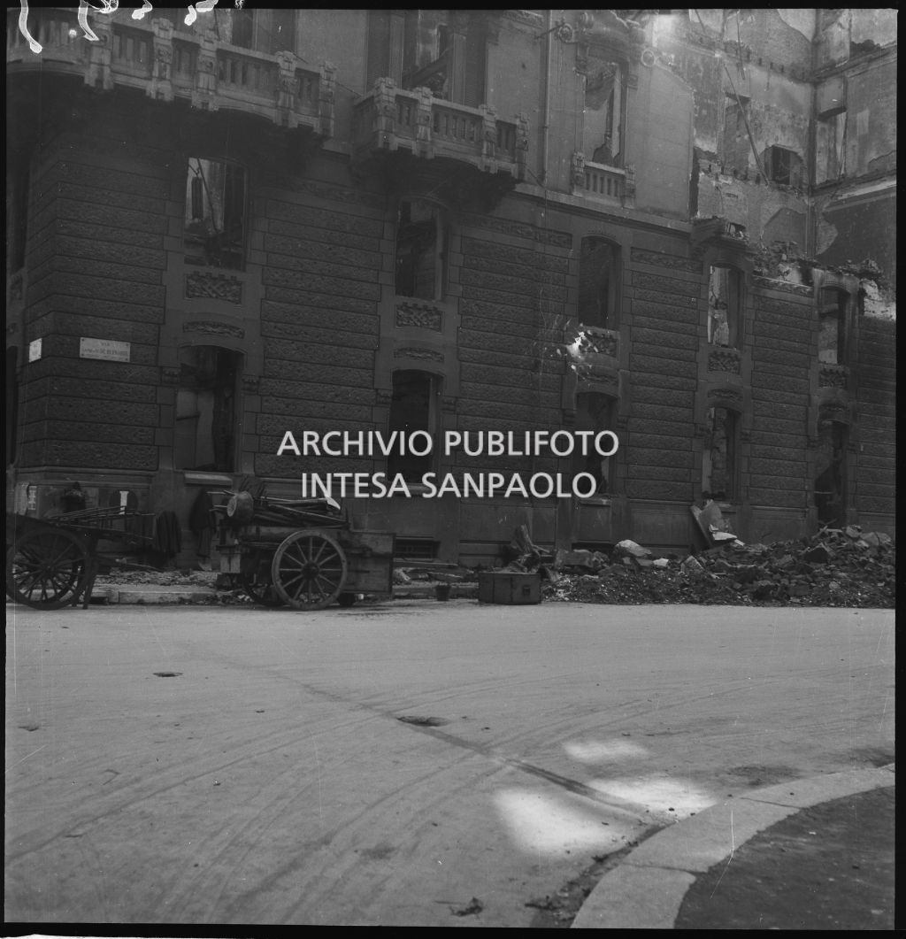 Esterno dell'edificio in viale Piave 15 all'angolo con via Lamberto De Bernardi, a Milano, sventrato dai bombardamenti; per strada macerie e due carretti a trazione umana. Sul muro il segnale "I" che indica l'attacco per l'idrante.
