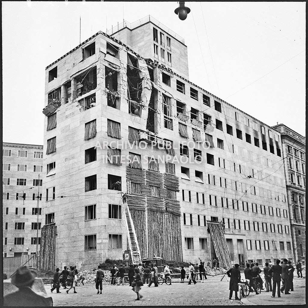 Passanti e militari assistono alle operazioni di messa in sicurezza, anche con l'aiuto di un'autoscala, di Palazzo Montecatini, in via della Moscova a Milano, gravemente danneggiato dai bombardamenti; i piani superiori sono sventrati e un pilastro è pericolante