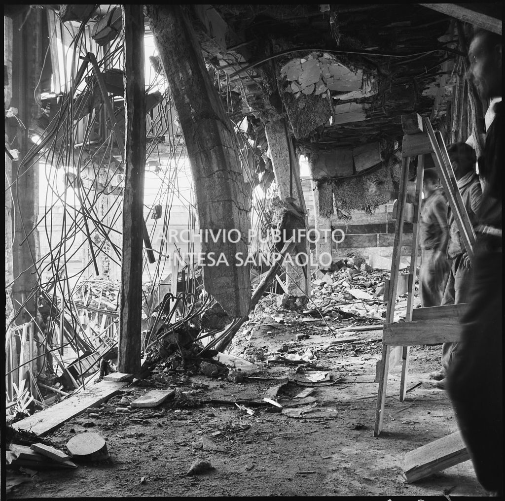 Interno di uno dei piani superiori di Palazzo Montecatini, in via della Moscova a Milano, sventrato dai bombardamenti, pericolante e ingombro di macerie; sulla destra si intravedono tre uomini