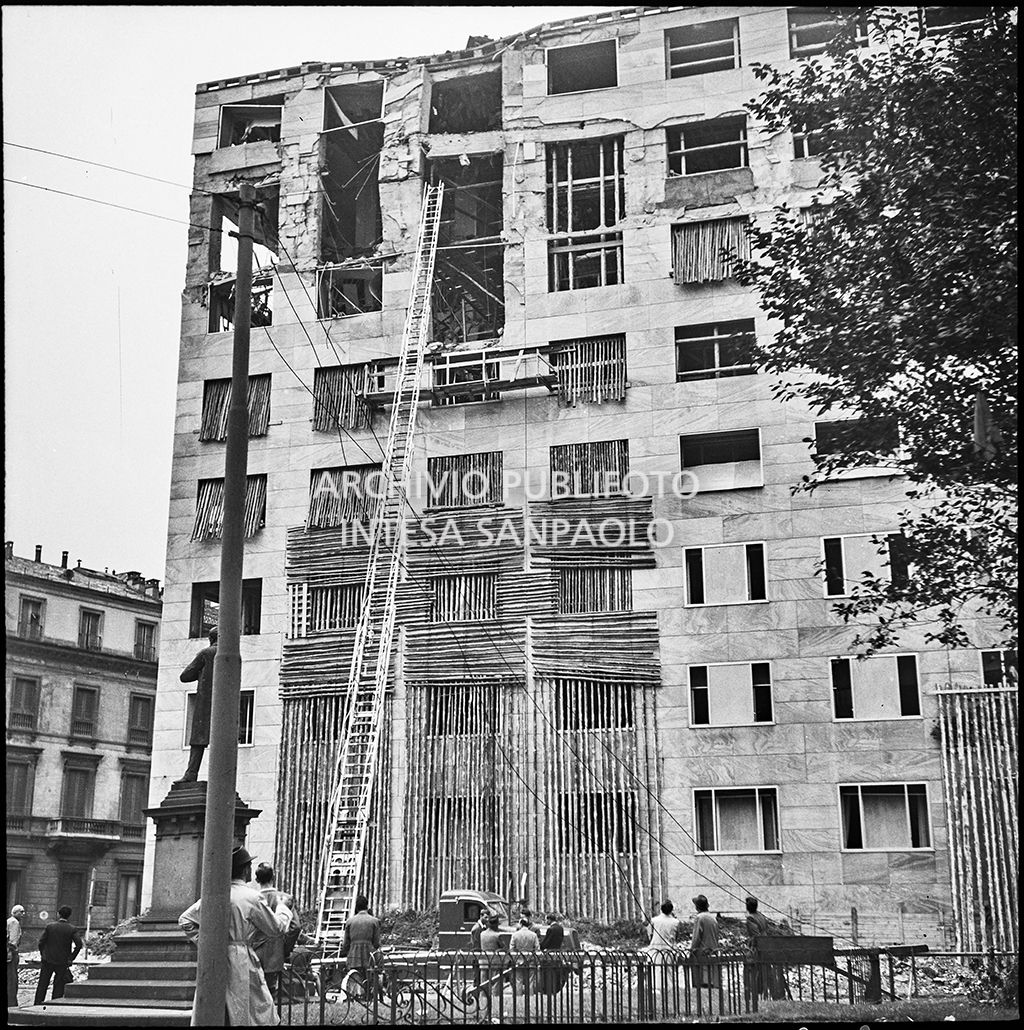 Passanti assistono alle operazioni di messa in sicurezza, anche con l'aiuto di un'autoscala, di Palazzo Montecatini, in via della Moscova a Milano, gravemente danneggiato dai bombardamenti; i piani superiori sono sventrati e un pilastro è pericolante