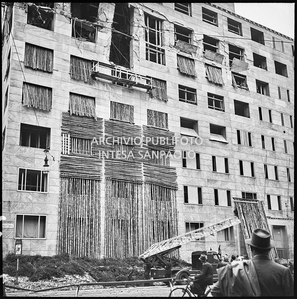 Passanti assistono alle operazioni di messa in sicurezza di Palazzo Montecatini, in via della Moscova a Milano, gravemente danneggiato dai bombardamenti; i piani superiori sono sventrati e un pilastro è pericolante