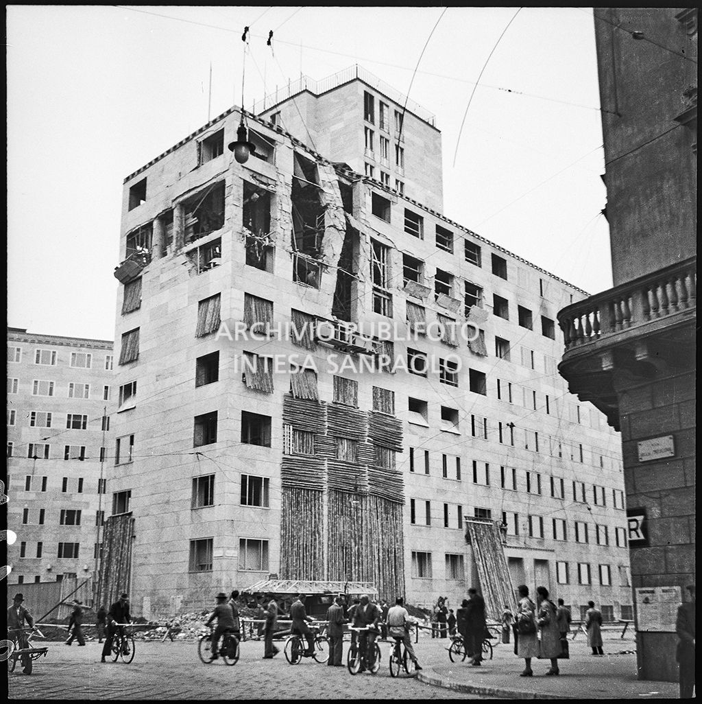Passanti assistono alla demolizione di un pilastro pericolante di Palazzo Montecatini, in via della Moscova a Milano, gravemente danneggiato dai bombardamenti. Sul muro a destra la freccia indicativa "R" per Rifugio-Ricovero antiaereo