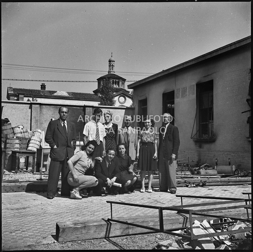 Foto di gruppo nel cortile dello stabilimento della Società anonima lavorazioni industriali (SALFI), in via Riccardo Pitteri a Milano, distrutto dai bombardamenti. Sullo sfondo la chiesa Santissimo Nome di Maria