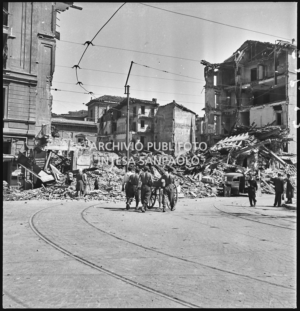 Quattro uomini spingono un carretto a mano verso le macerie degli edifici di via Alciato, a Milano, distrutti dai bombardamenti