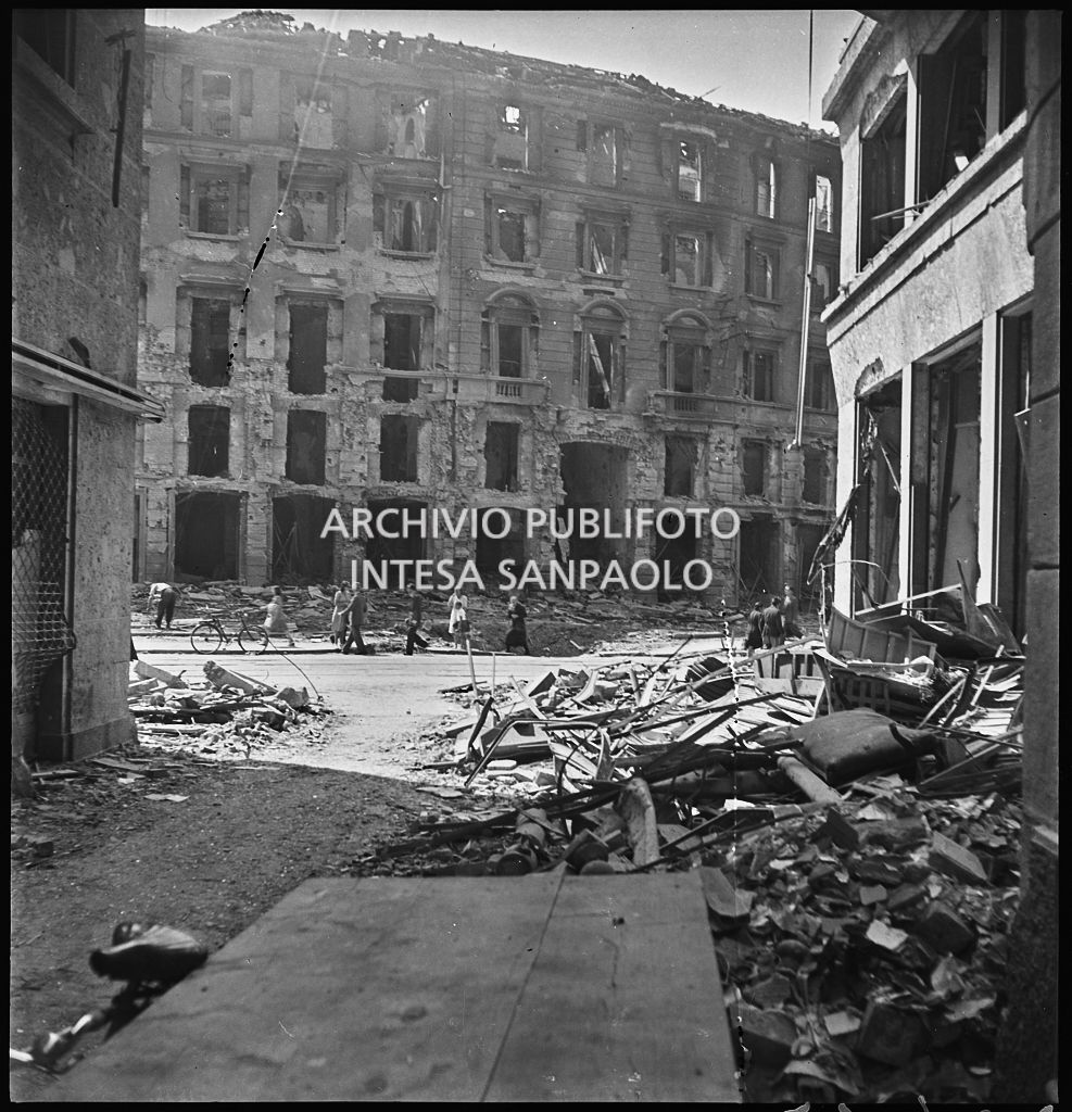 Scorcio di un edificio in largo Augusto, a Milano, gravemente danneggiato dai bombardamenti; alcuni passanti per strada