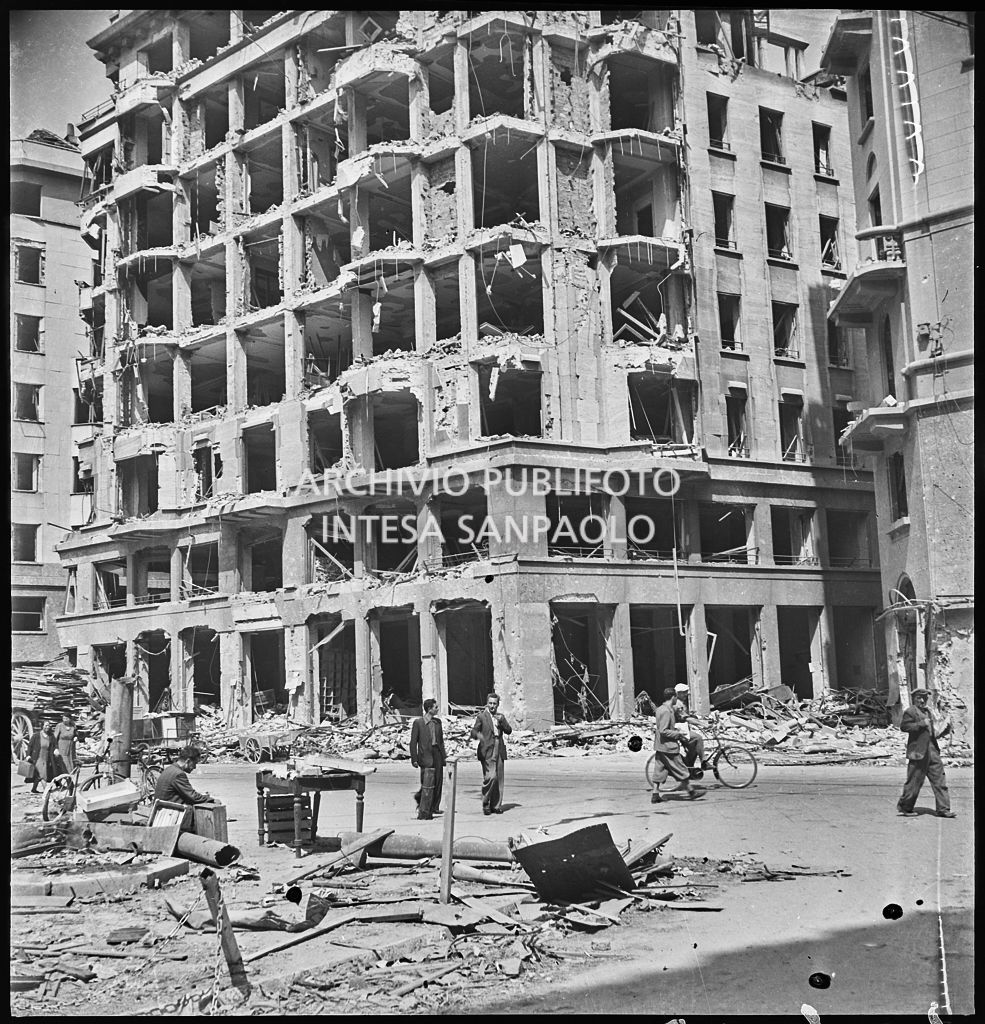 Edificio in largo Augusto all'angolo con via Marziale, a Milano, sventrato dai bombardamenti; per strada passanti, masserizie e macerie