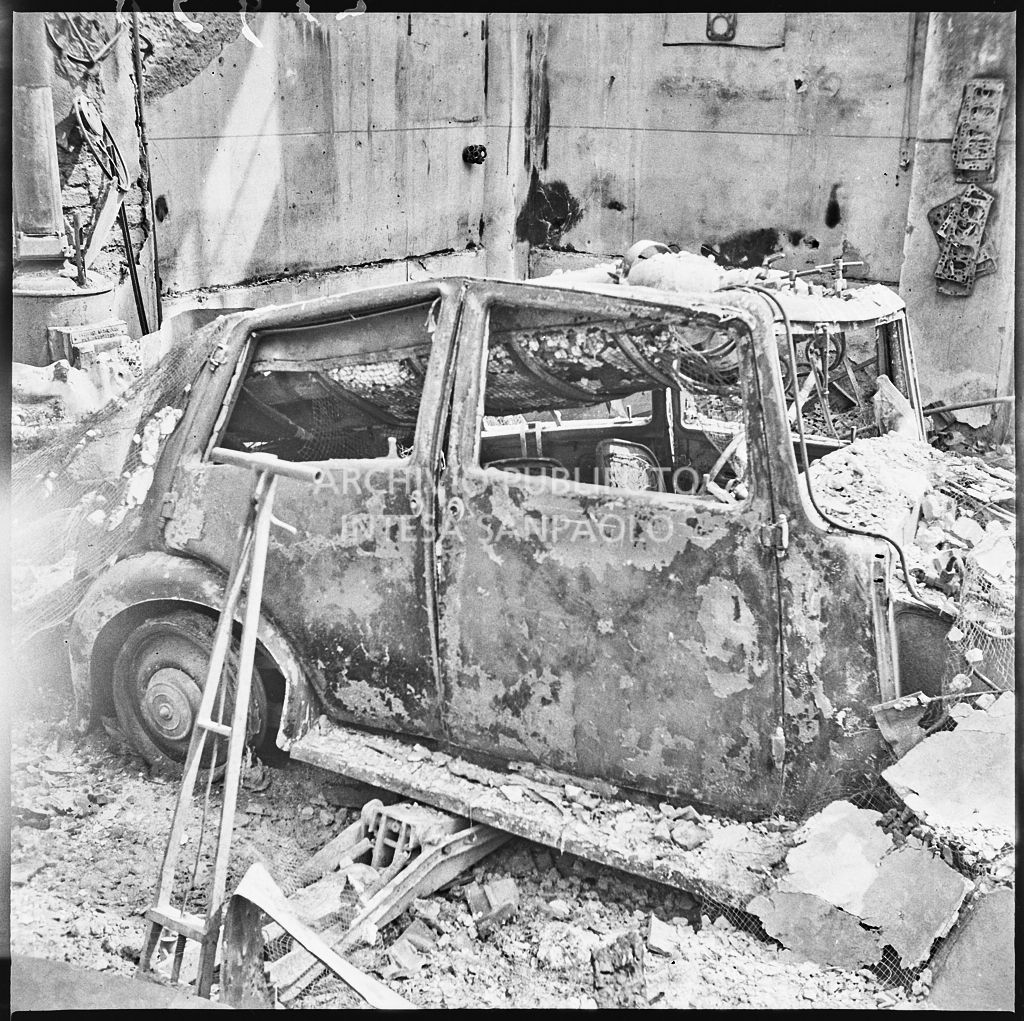 Un'automobile bruciata a causa dei bombardamenti, a Milano, all'interno di un edificio ingombro di macerie