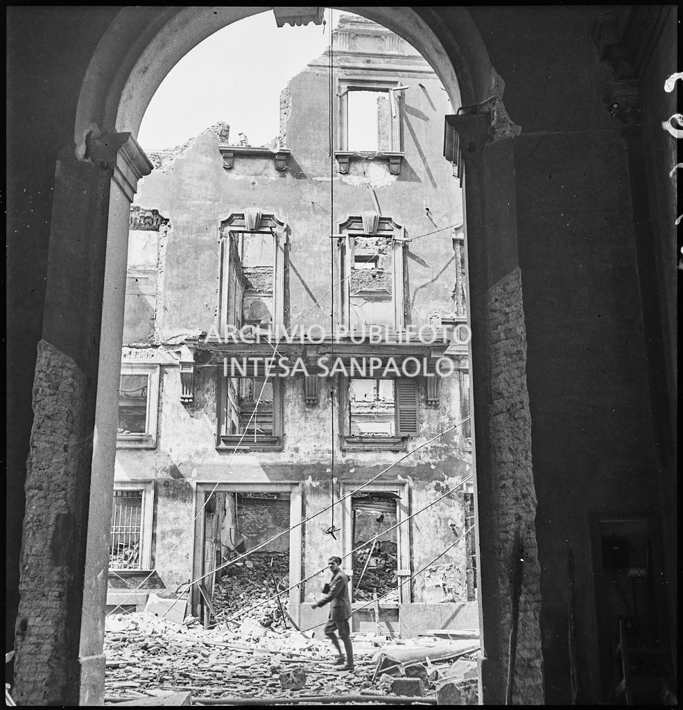 Un palazzo in via Brera, a Milano, sventrato dai bombardamenti; in primo piano un uomo cammina sulle macerie