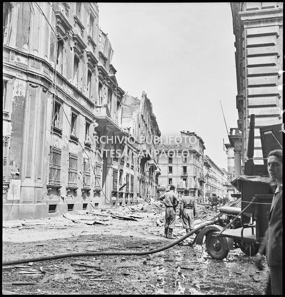 Scorcio di via Brera, a Milano, ingombra di macerie dopo i bombardamenti; sulla destra un mezzo dei vigili del fuoco, al centro un militare e un pompiere osservano la devastazione della via