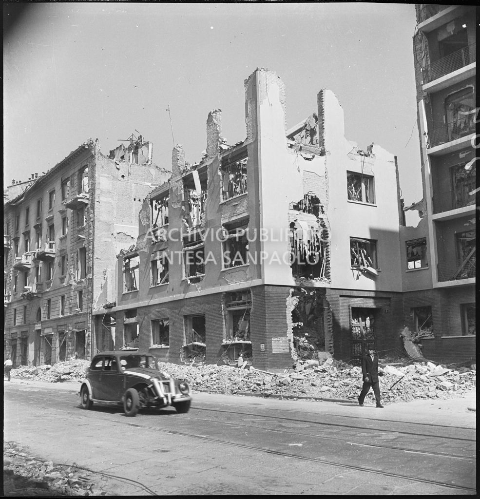 Scorcio di viale Coni Zugna, a Milano, con gli edifici sventrati dai bombardamenti; al centro della strada un'automobile con la fasce bianche per renderla più visibile durante l'oscuramento, a lato un passante