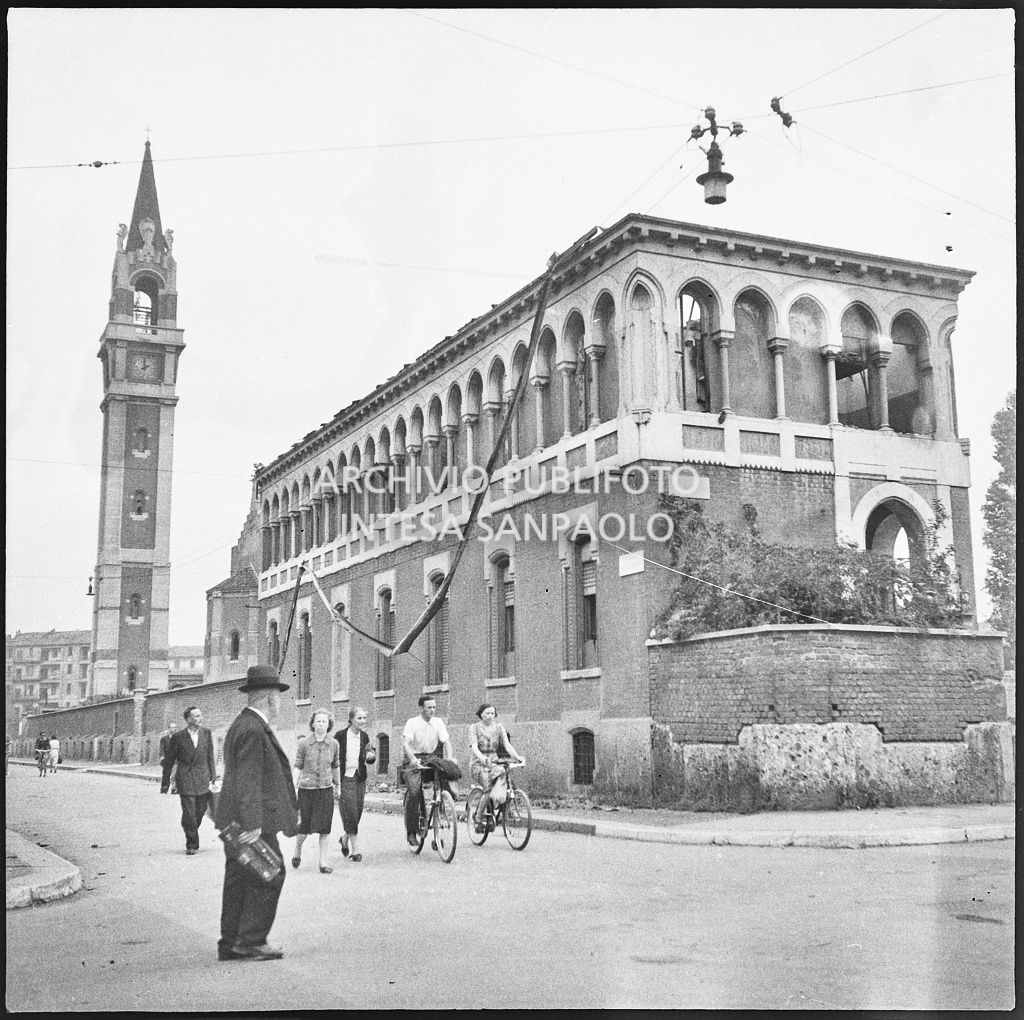 Passanti in via Paolo Lomazzo, a Milano, all'incrocio con via Monviso, a piedi e in bicicletta, dopo i bombardamenti della città. Sullo sfondo la basilica Prepositurale di Santa Maria di Lourdes