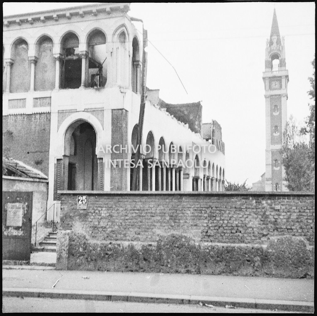 Passanti in via Paolo Lomazzo, a Milano, all'incrocio con via Monviso, a piedi e in bicicletta, dopo i bombardamenti della città. Sullo sfondo la basilica Prepositurale di Santa Maria di Lourdes