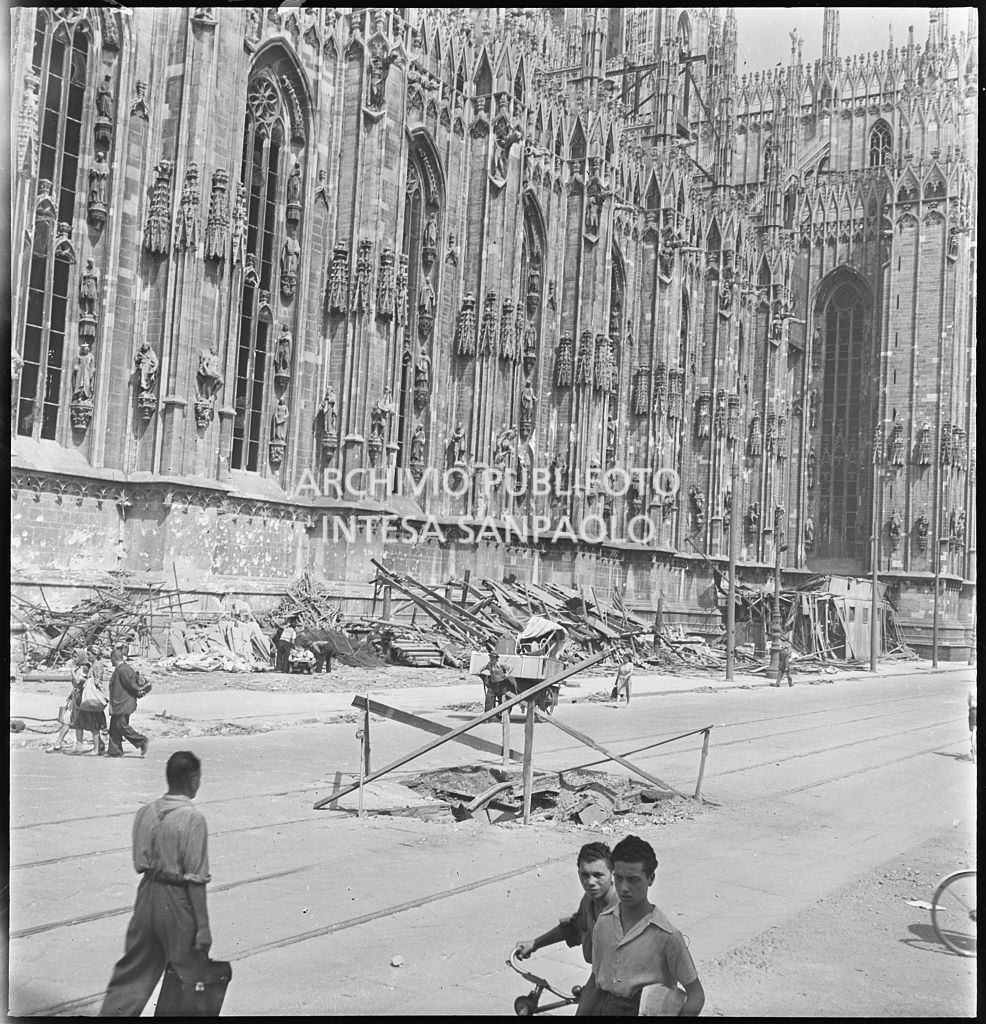 Voragine, in piazza del Duomo a Milano, causata dai bombardamenti e transennata con assi di legno. A ridosso del lato sud del Duomo sono ammucchiate macerie