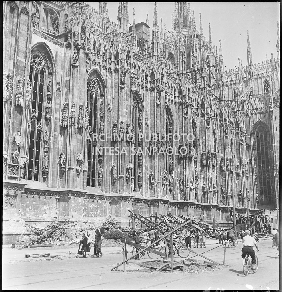 Voragine, in piazza del Duomo a Milano, causata dai bombardamenti e transennata con assi di legno. A ridosso del lato sud del Duomo sono ammucchiate macerie