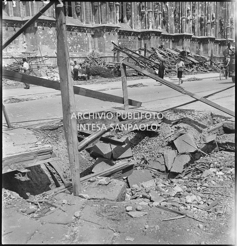 Voragine, in piazza del Duomo a Milano, causata dai bombardamenti e transennata con assi di legno. A ridosso del lato sud del Duomo sono ammucchiate macerie
