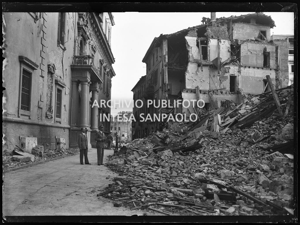 Scorcio di piazza Cesare Beccaria, a Milano, dopo i bombardamenti che hanno gravemente danneggiato il Palazzo del Capitano, allora tribunale della città, e ridotto in macerie gli edifici circostanti. Due uomini tra cui un militare osservano il cumulo di macerie