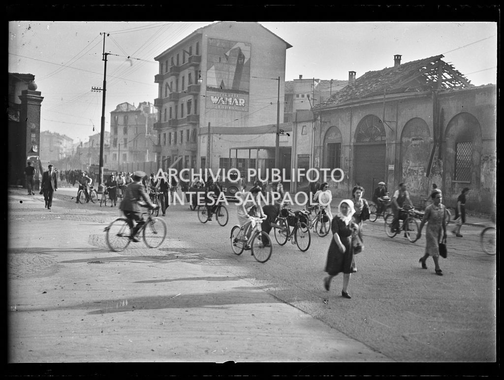 Persone, a piedi e in bicicletta, in via Carlo Farini a Milano, lasciano la città dopo i bombardamenti