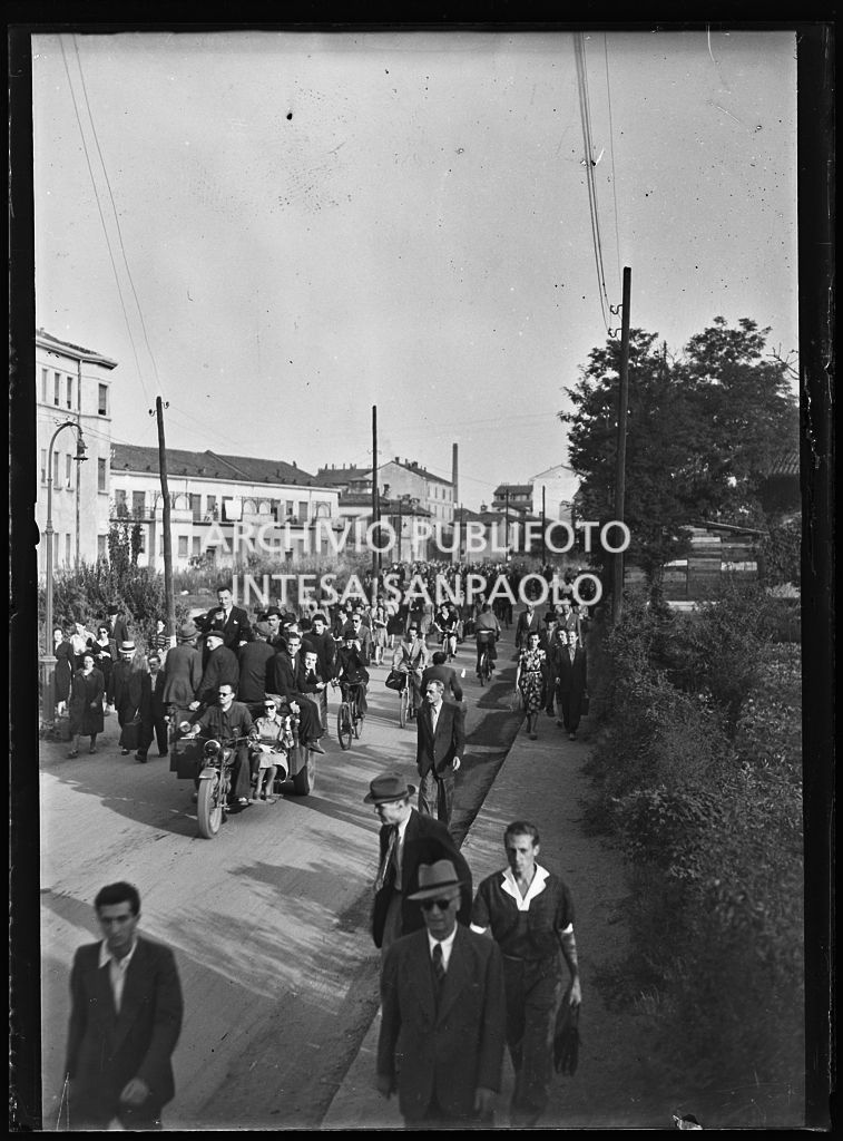 Persone, in una via di Milano nei giorni dei bombardamenti, lasciano la città con ogni mezzo: a piedi, in bicicletta, su motocarri