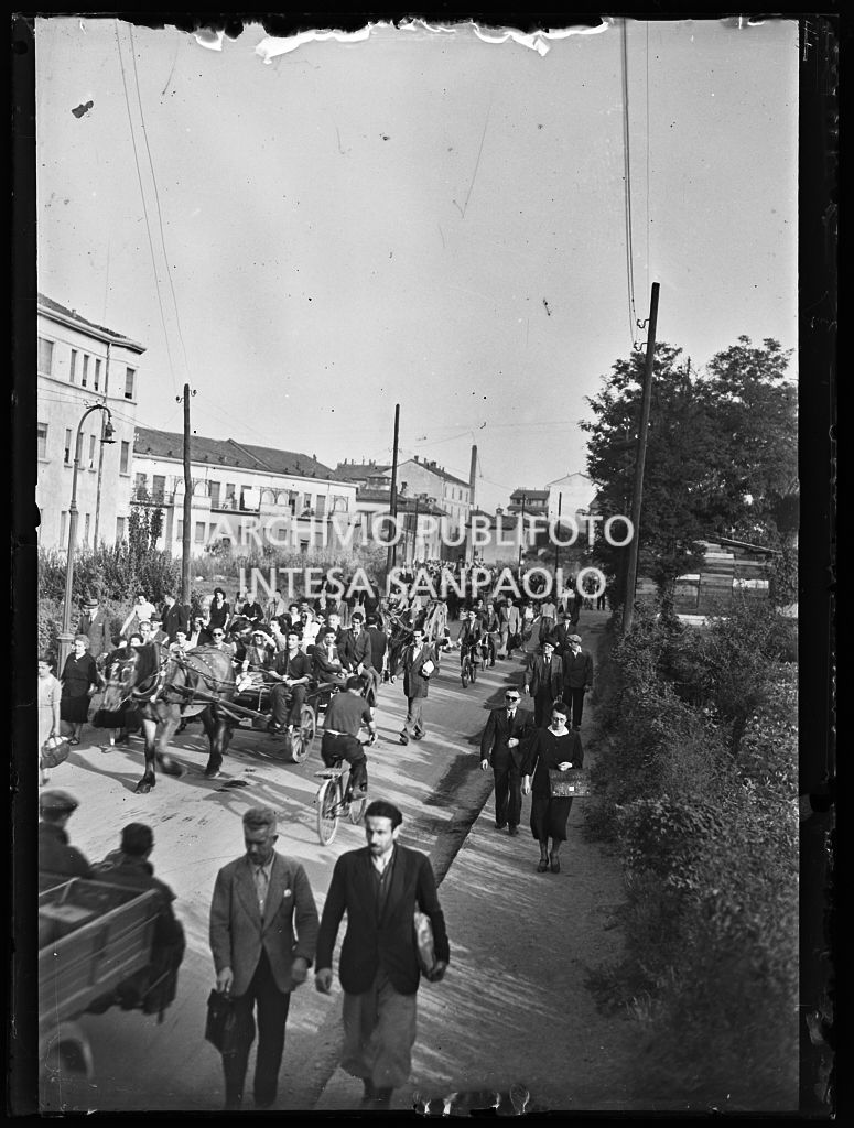 Persone, in una via di Milano nei giorni dei bombardamenti, lasciano la città con ogni mezzo: a piedi, in bicicletta, su carri trainati da cavalli