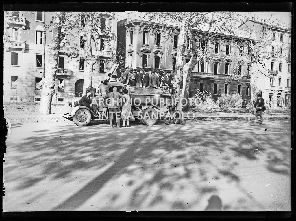 Un autocarro carico di persone, in un viale di Milano, dopo i bombardamenti della città