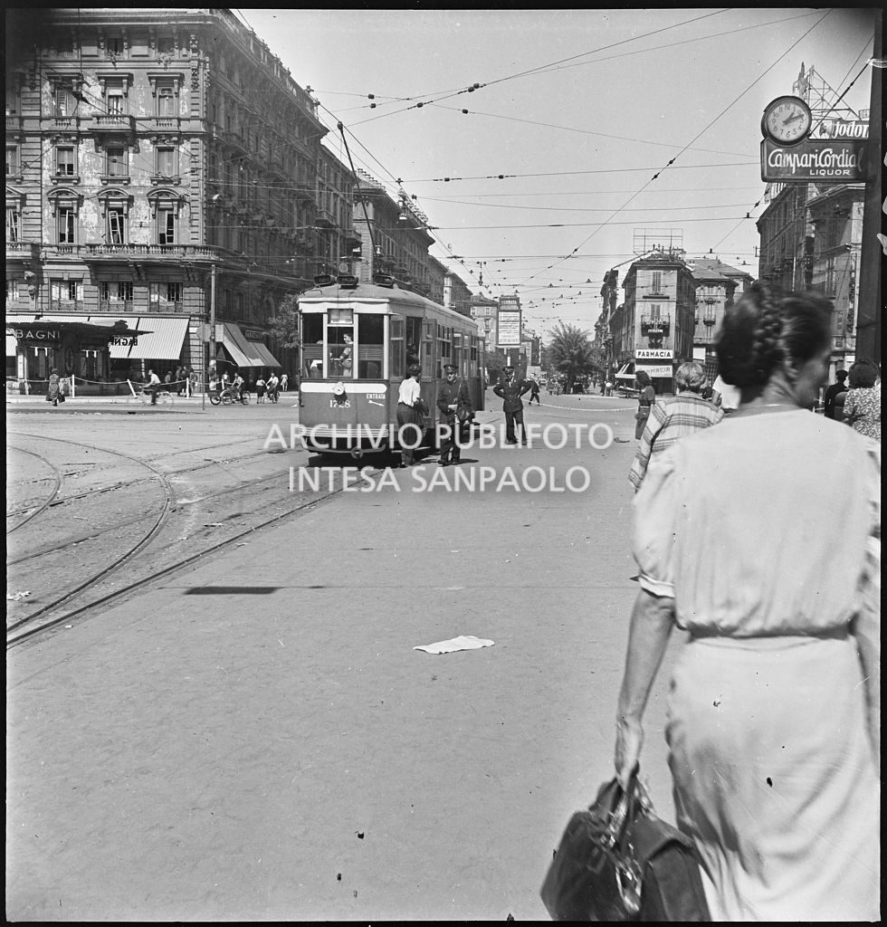 Scorcio di piazza Oberdan a Milano nei giorni dei bombardamenti della città. Alla fermata un tram tipo 1928 in sosta con le porte aperte e due controllori a terra.