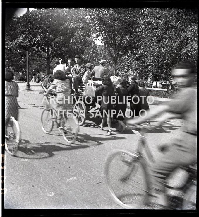 Esodo dalla città, dopo i bombardamenti di Milano, con un carro trainato da un cavallo, ai Bastioni di Porta Venezia: le donne a piedi, gli uomini a bordo. Molti altri si spostano in bicicletta