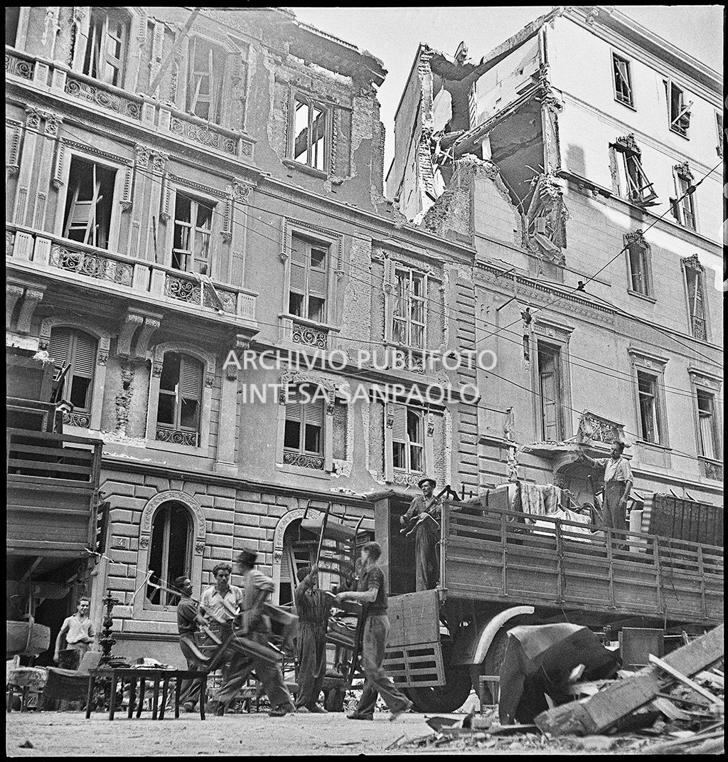 Uomini caricano un camion di masserizie recuperate dalle abitazioni bombardate, davanti a un edificio sventrato a Milano